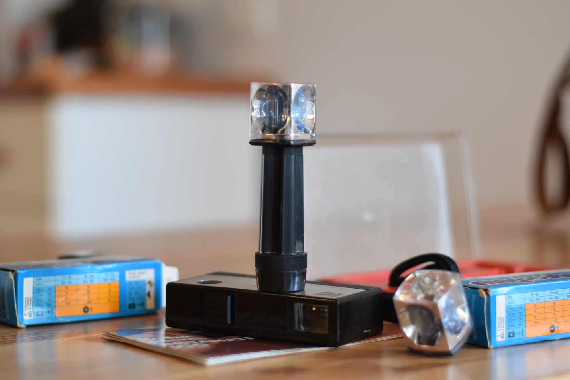 Magicube flash unit with four single-use flash bulbs. Attached to camera directly or with provided extension pole. Magicube is small and silver with a clear plastic cover, two boxes of Magicubes are shown in the background