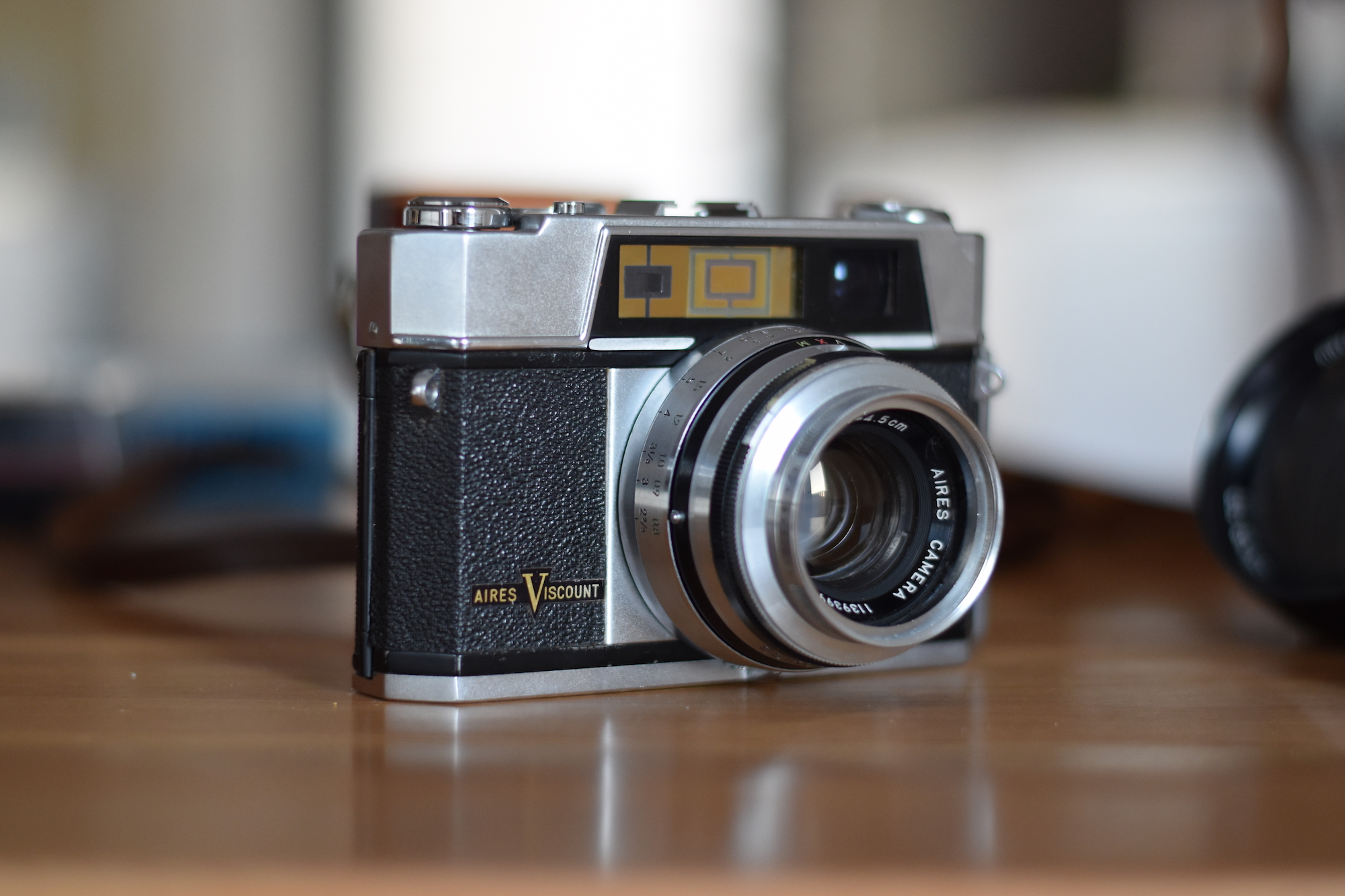 An Aires Viscount rangefinder camera. The base is silvery, the body black leatheret and the top is silvery.