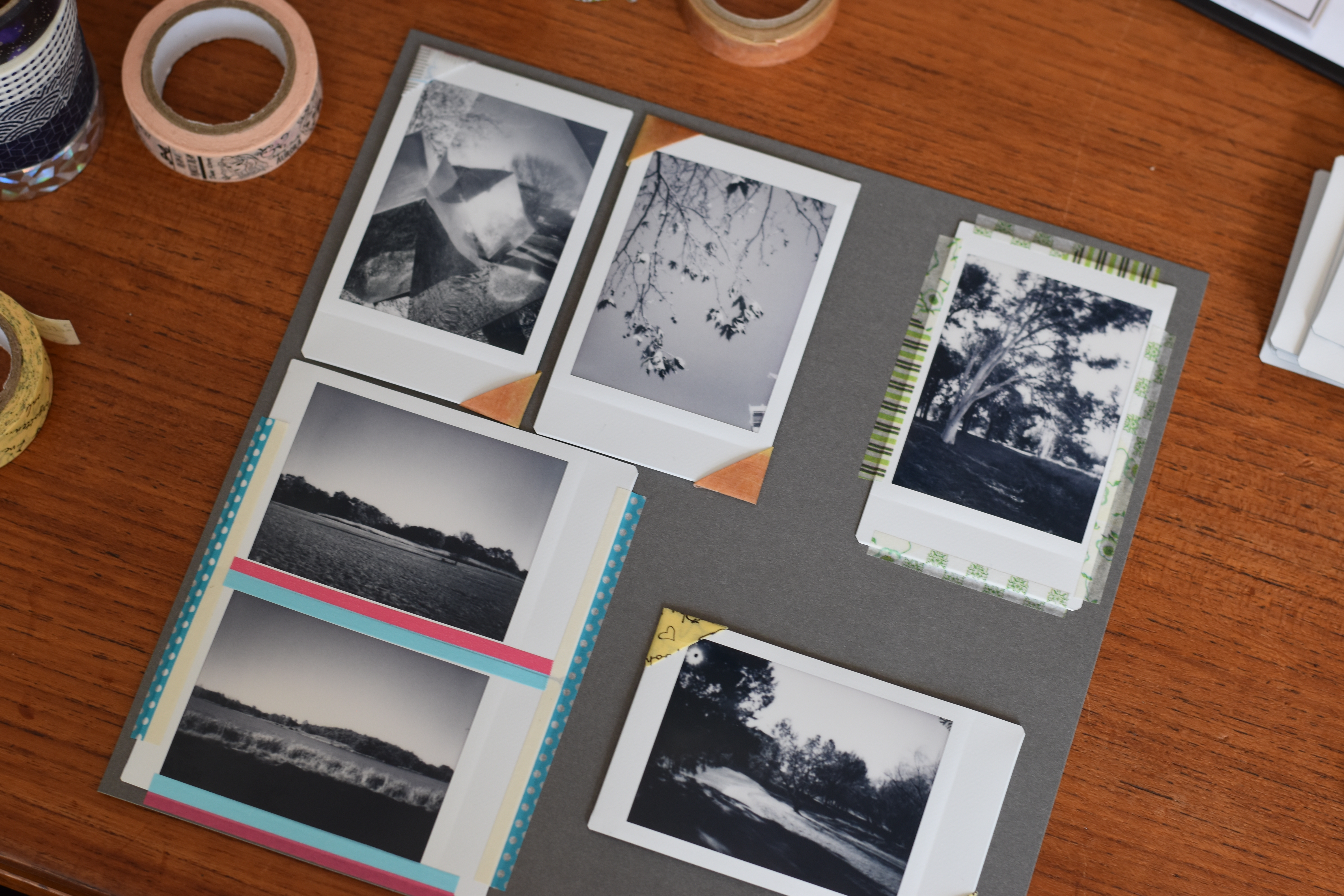 A page from a scrapbook with 6 Instax mini photos. From top left, a print has photo corners on two corners, a print has photo corners on two corners, a print is held down by tape on four sides, a print has photo corners on two corners, two prints are taped by tape on three sides